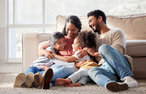 Family with dad, mom, and two kids sitting on the living room floor